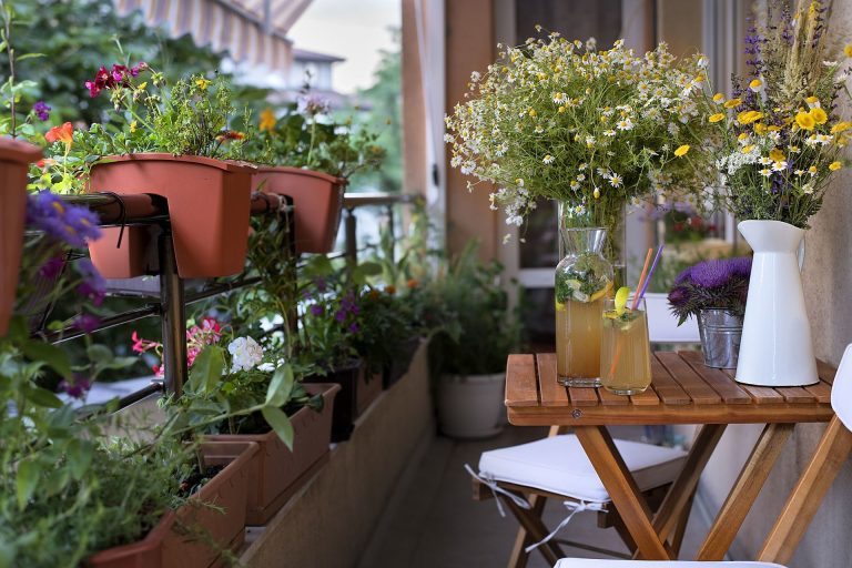 Balcón con macetas de flores, mesa de madera y jarrones con arreglos florales.