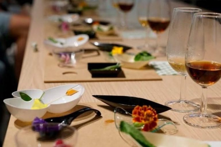 Mesa servida con platos decorativos, flores comestibles y copas de bebida.